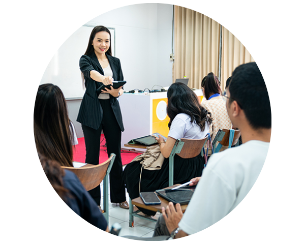 A professional woman in a black suit leads a discussion in a classroom, engaging with seated students.