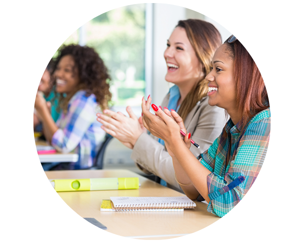 A diverse group of women in a classroom claps and smiles while engaging in a learning session.